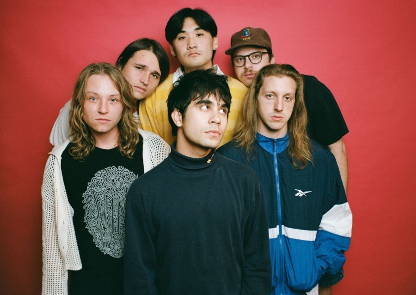 The six members of the band The Sophs in front of a red backdropx